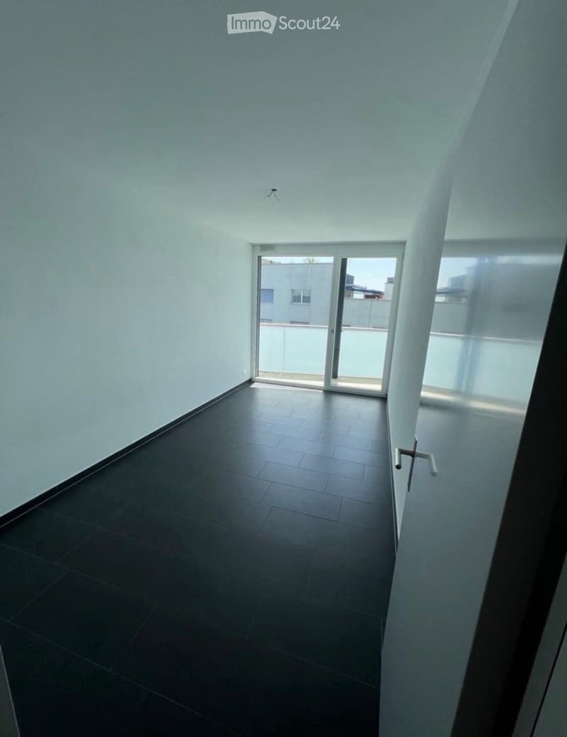 Empty room with dark tiled floor and white walls, featuring a sliding glass door leading to a balcony area.