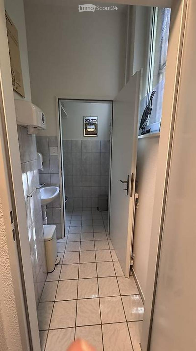 Modern bathroom with white tiled walls and floor, a sink, toilet, shower area, and a small window with a view of the outside.