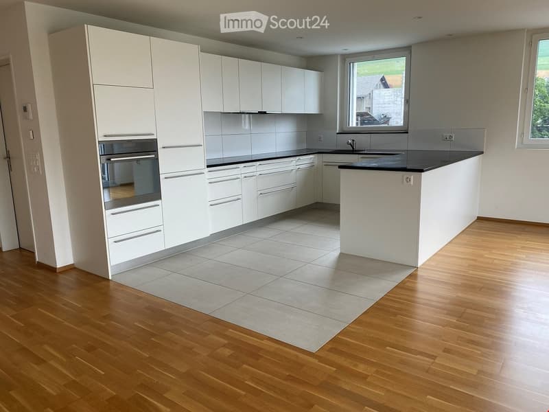 Modern kitchen with white cabinets, stainless steel oven, black countertop, and a central island with sink.