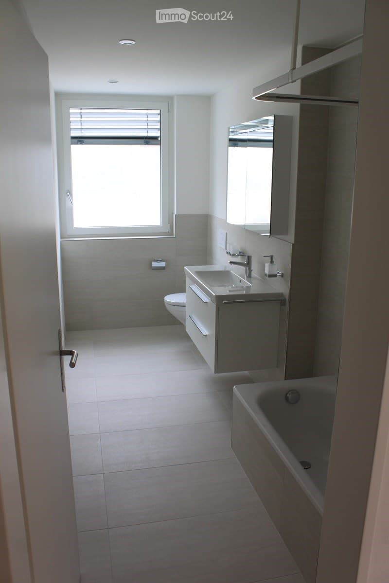 Modern bathroom with white tiles, a large window, a sink with a faucet, a toilet, a bathtub, and a mirrored cabinet.