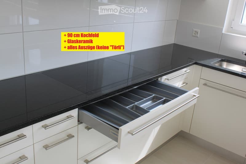 Modern kitchen with white cabinets, black countertop, and a large open drawer with multiple compartments.