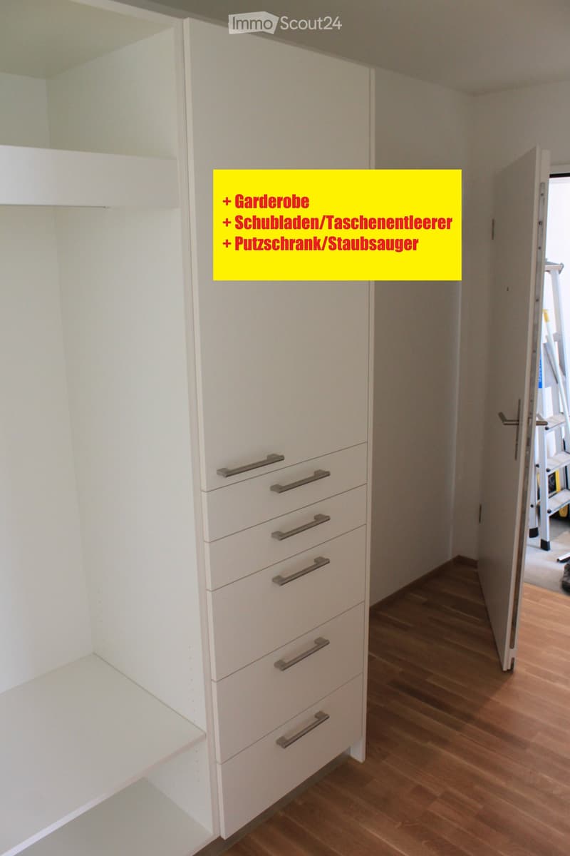 Empty room with white built-in wardrobe and drawers, wooden flooring, and an open doorway leading to another area.