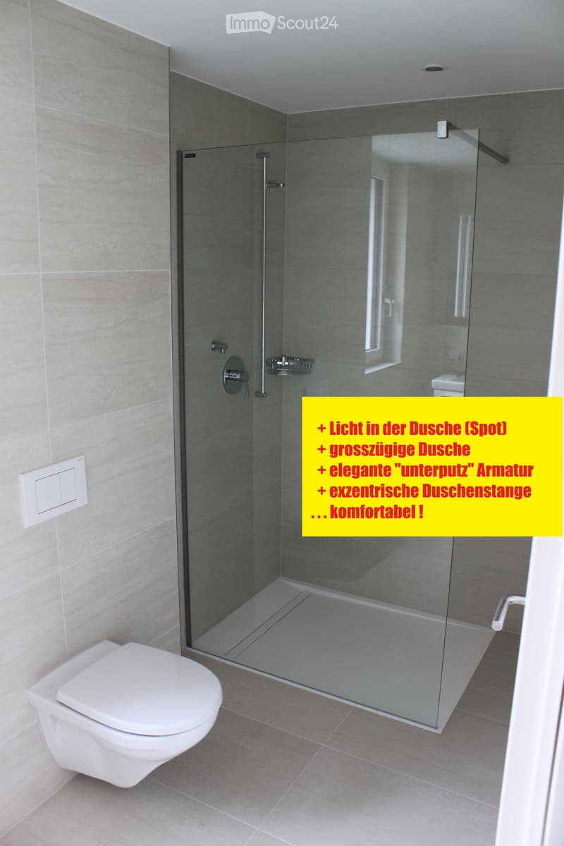 Modern bathroom with a glass-enclosed shower stall, toilet, and sleek faucet. Light-colored tiles on walls and floor.
