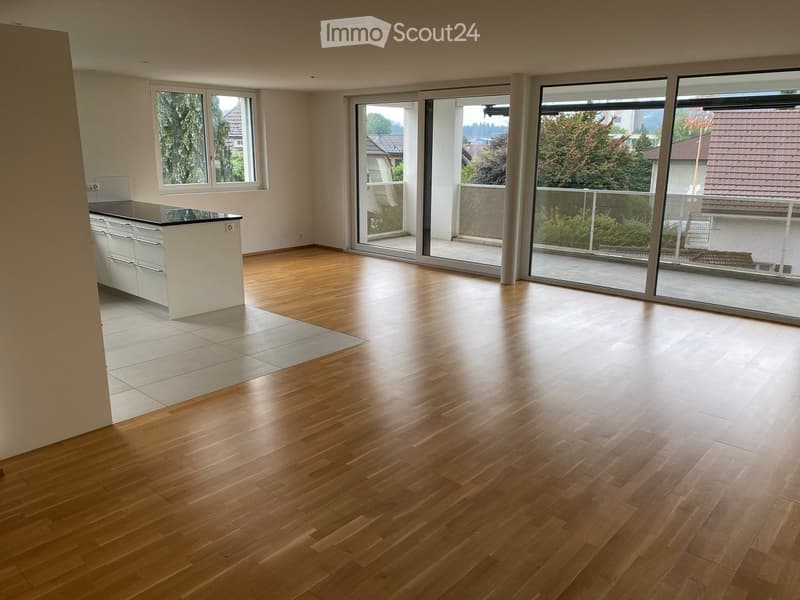 Empty room with wooden flooring, white walls, large windows, and sliding glass doors leading to a balcony.