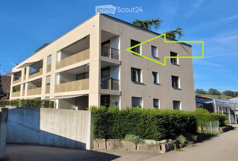 Modern multi-story residential building with balconies, large windows, and a landscaped front yard.