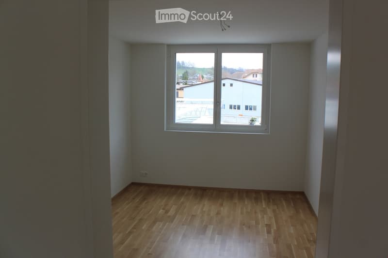 Empty room with wooden flooring and a large window offering a view of the outside area.