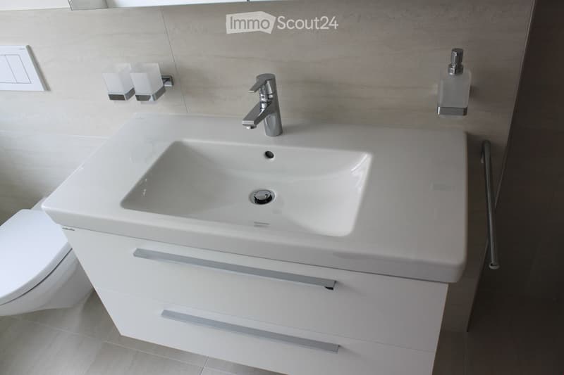 Modern bathroom with a white sink, chrome faucet, built-in cabinet, toilet, and soap dispenser.
