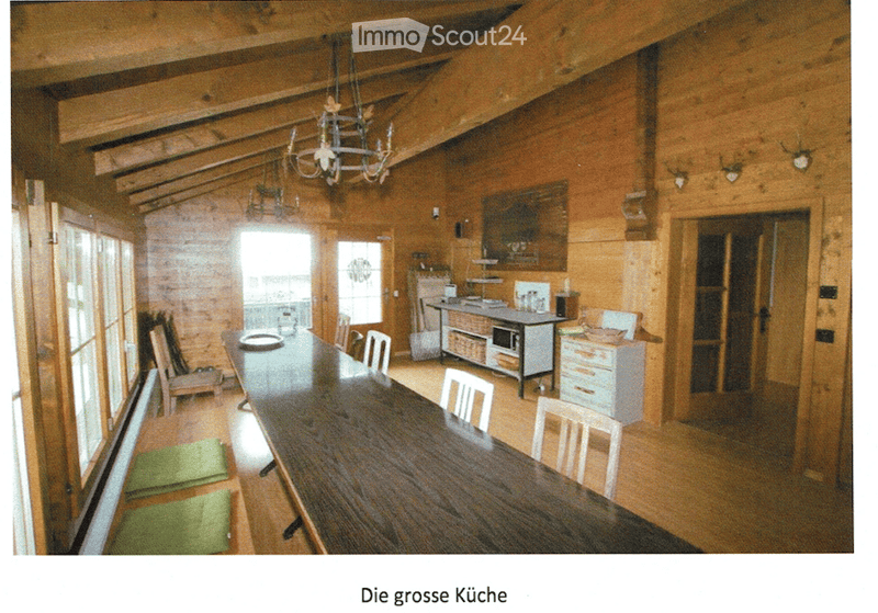 A spacious, wooden-paneled dining area with a long wooden dining table surrounded by chairs, a small kitchen area with cabinets and a microwave, and a chandelier hanging from the ceiling.