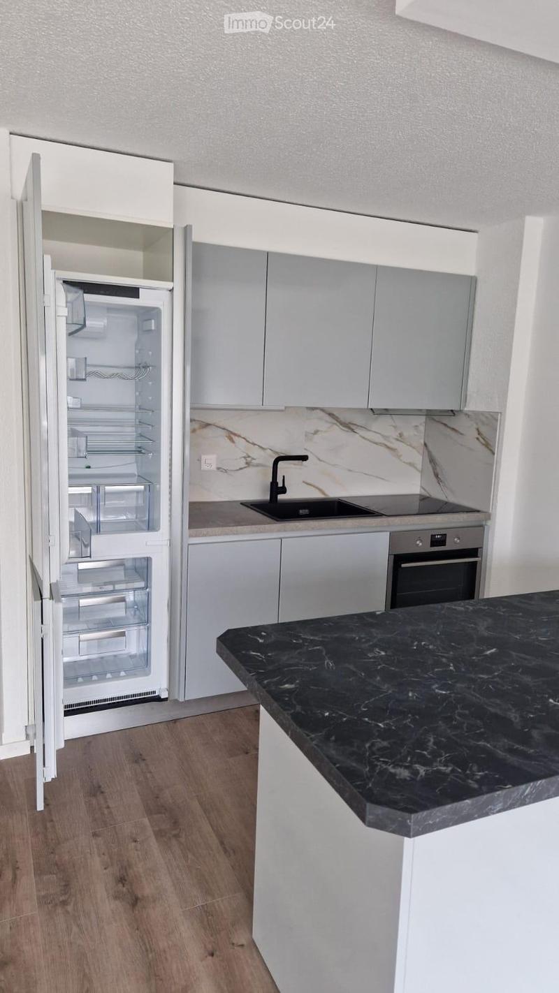 Modern kitchen with white cabinets, black marble countertop, stainless steel sink, and open refrigerator.