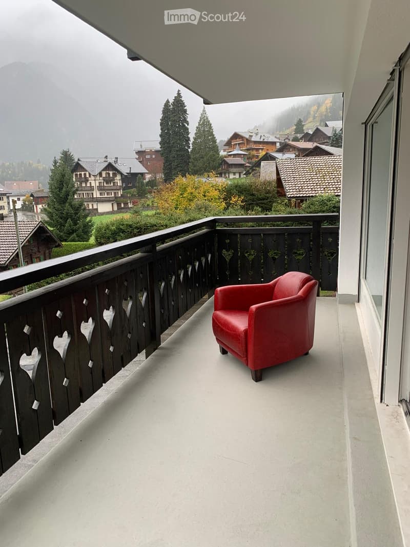 Balcony with a red leather chair, wooden railing, and scenic mountain view.