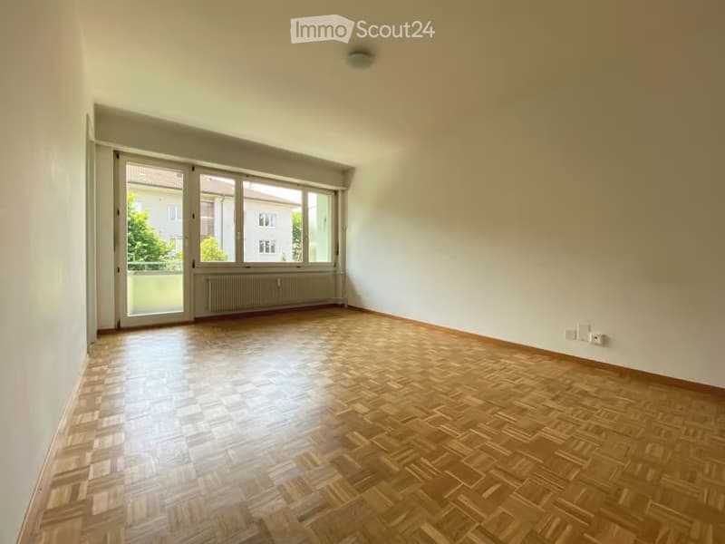 Empty room with wooden parquet flooring, large windows, and white walls. No furniture or equipment present.