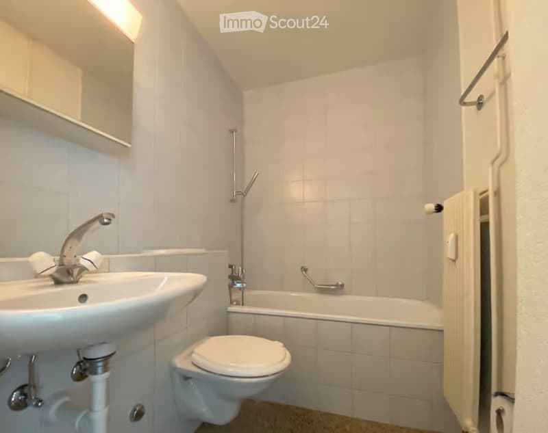 Modern bathroom with white tiles, a sink, toilet, bathtub, and a mirror above the sink.