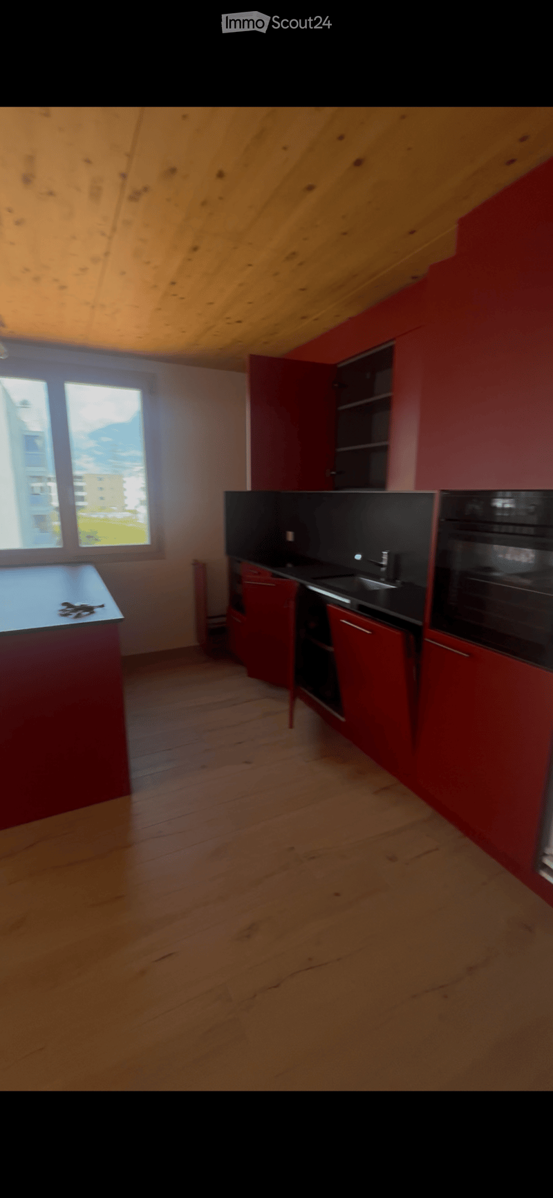 Modern kitchen with red cabinets, black countertops, and a large window offering a view of the outdoors.