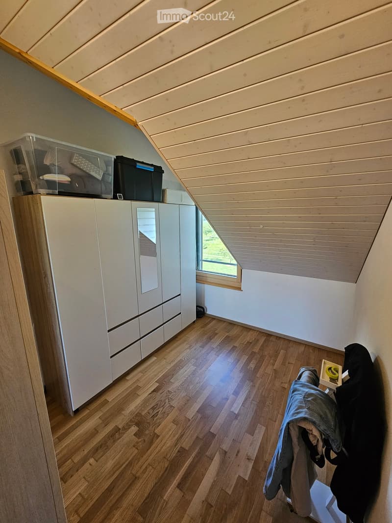 A small, well-lit room with wooden flooring and white walls, featuring a built-in wardrobe and storage boxes on top.