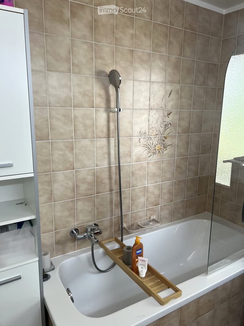 Bathroom with a bathtub, wooden tray holding toiletries, showerhead, faucet, and a white cabinet.