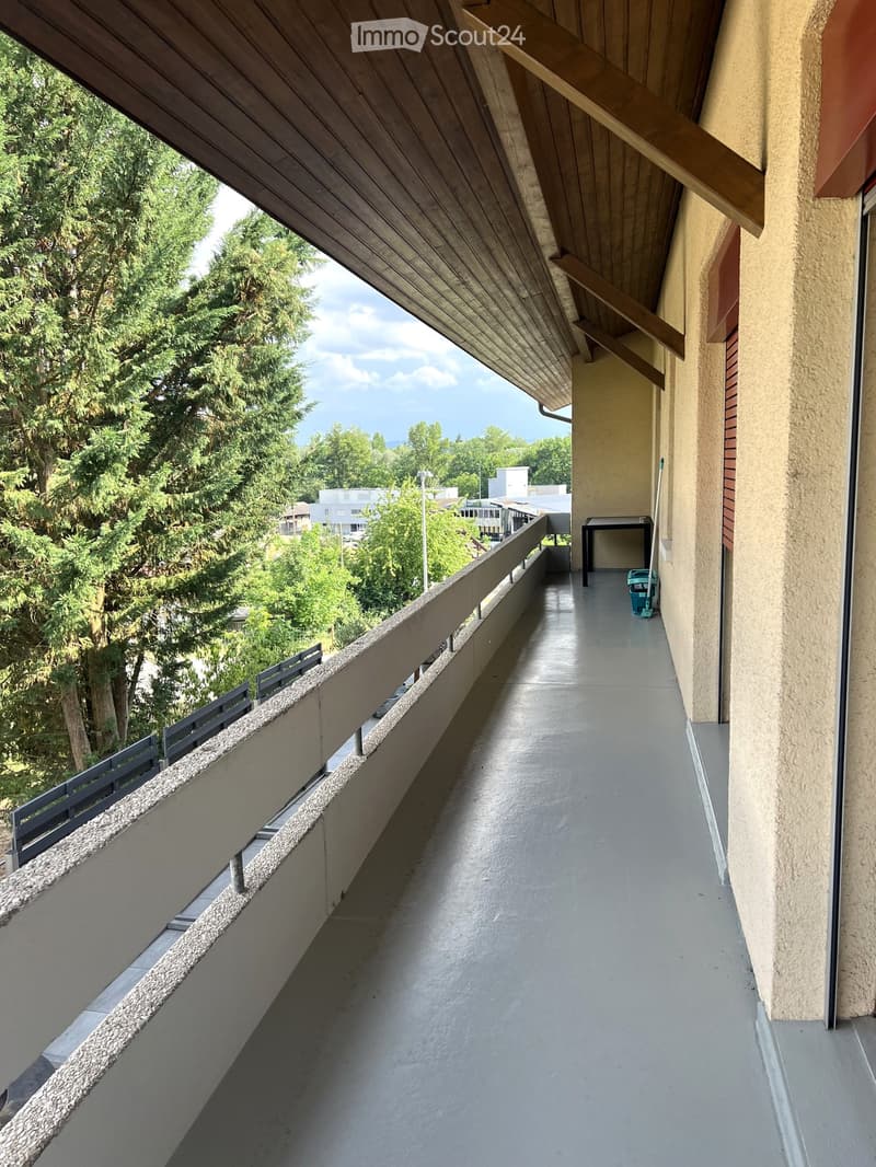 Balcony with wooden ceiling, concrete floor, metal railing, and a view of trees and buildings.