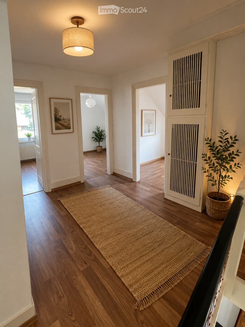 A well-lit hallway with wooden flooring, a woven runner rug, and several doors leading to different rooms. The walls are painted in a light neutral color, and there are framed pictures and potted plants visible in the adjacent rooms.