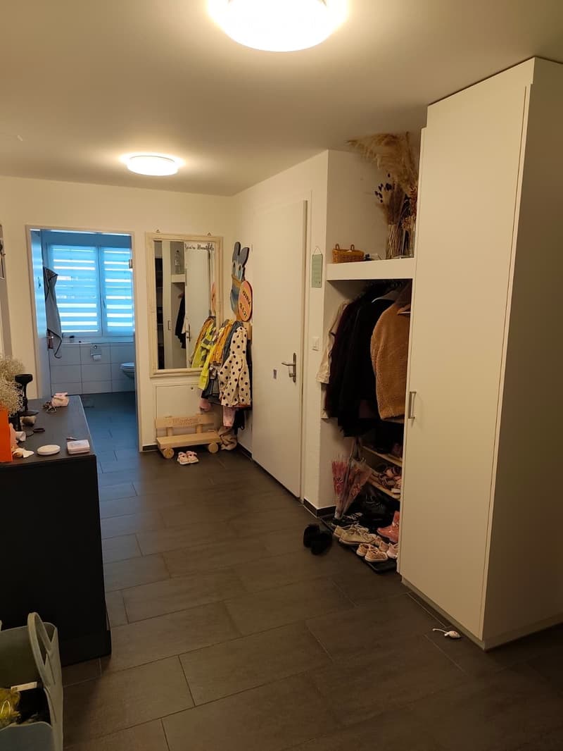 Hallway with tiled floor, built-in closet, coat rack, small table, and a view into a bathroom.