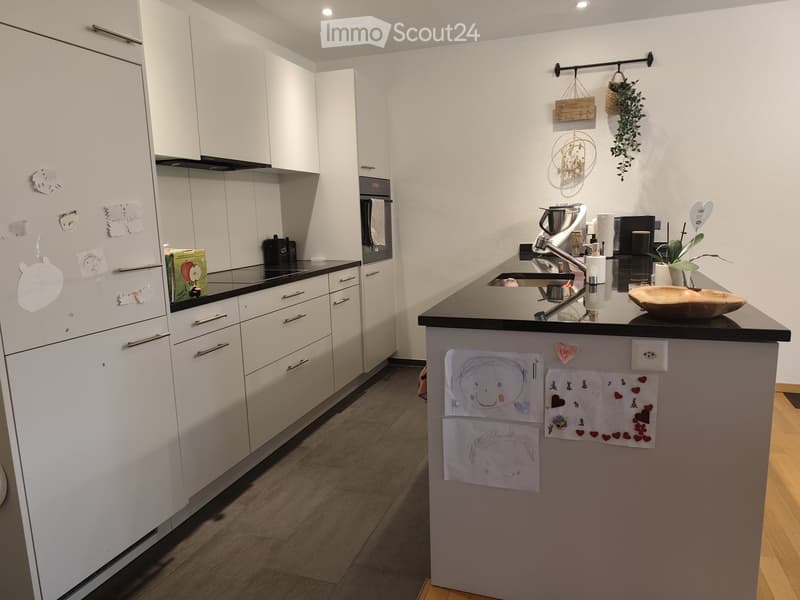 Modern kitchen with white cabinets, black countertops, and various appliances including a refrigerator, oven, and sink. The island features drawings and decorations.