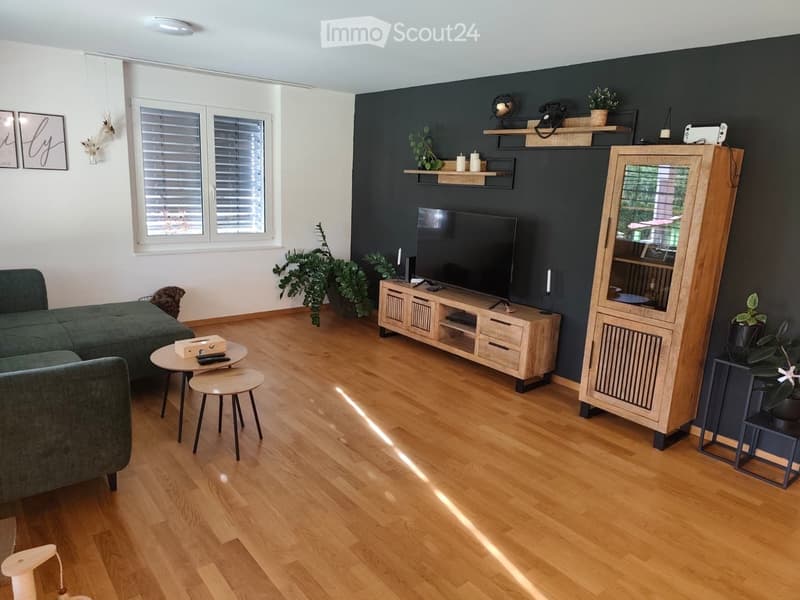 Modern living room with wooden flooring, dark green sofa, coffee table, TV stand, and decorative shelves.