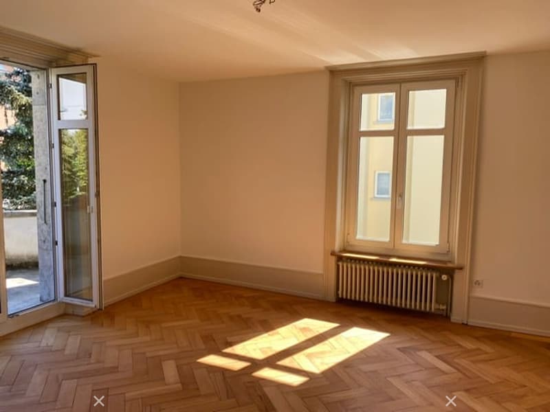 Empty room with wooden flooring, large windows, and a radiator. No furniture or equipment present.