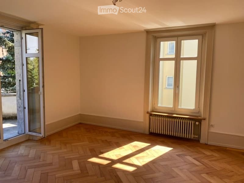 Empty room with wooden flooring, large windows, and a radiator. No furniture or equipment present.