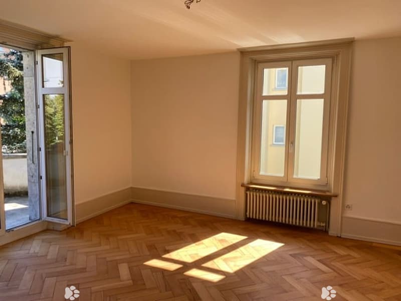 Empty room with wooden flooring, large windows, and a radiator. No furniture or equipment present.