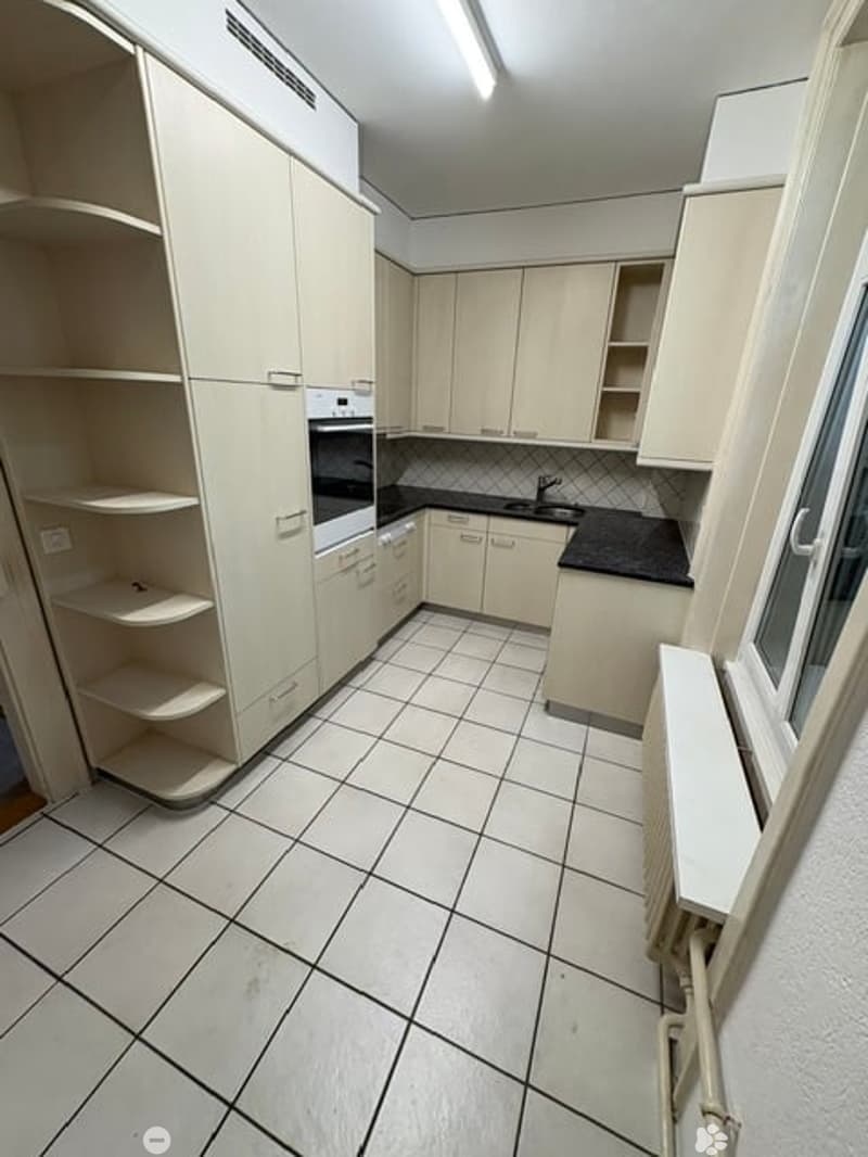 Modern kitchen with white cabinets, black countertops, and tiled flooring. Features an oven, sink, and faucet.