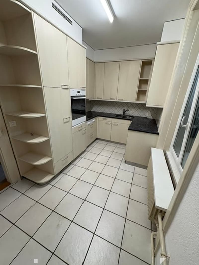 Modern kitchen with white cabinets, black countertops, and tiled flooring. Features an oven, sink, and faucet.