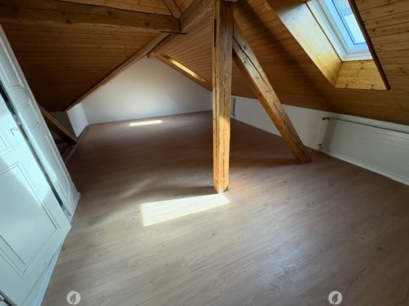 Empty attic room with wooden beams, wooden floor, and skylight window allowing natural light.