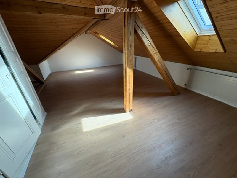 Empty attic room with wooden beams, wooden floor, and skylight window allowing natural light.