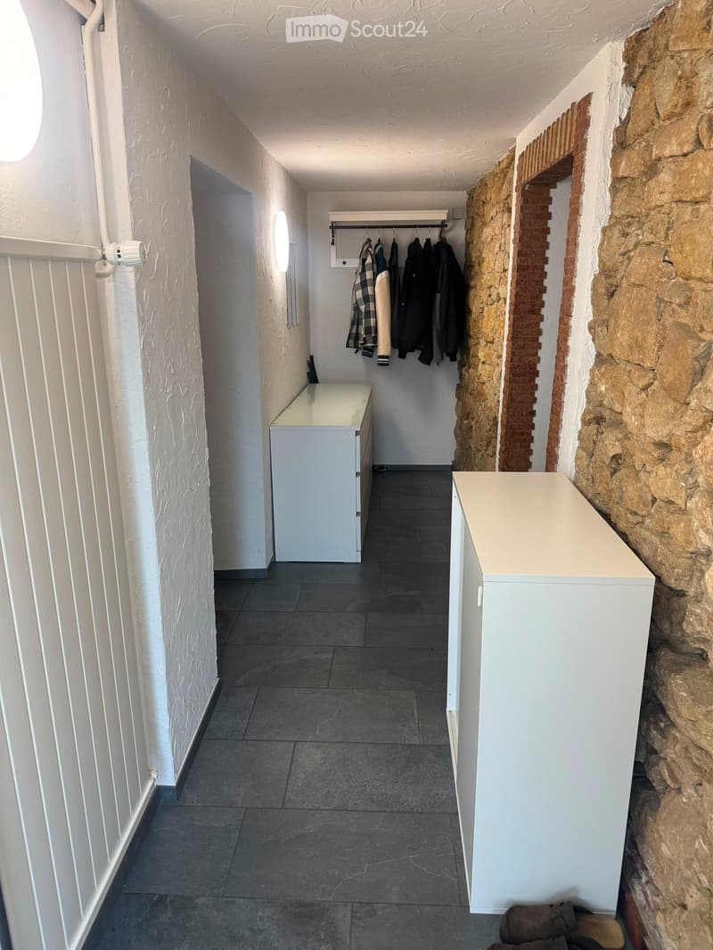 Narrow hallway with white walls, dark tiled floor, built-in coat rack, and small white console tables on both sides.