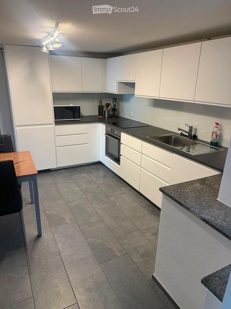 Modern kitchen with white cabinets, granite countertops, stainless steel sink, microwave, and oven. Includes a small dining area with a table and chairs.
