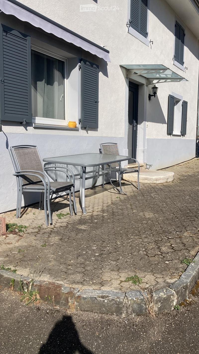 Outdoor seating area with a metal table and four chairs, situated next to a building with shutters and a small awning.