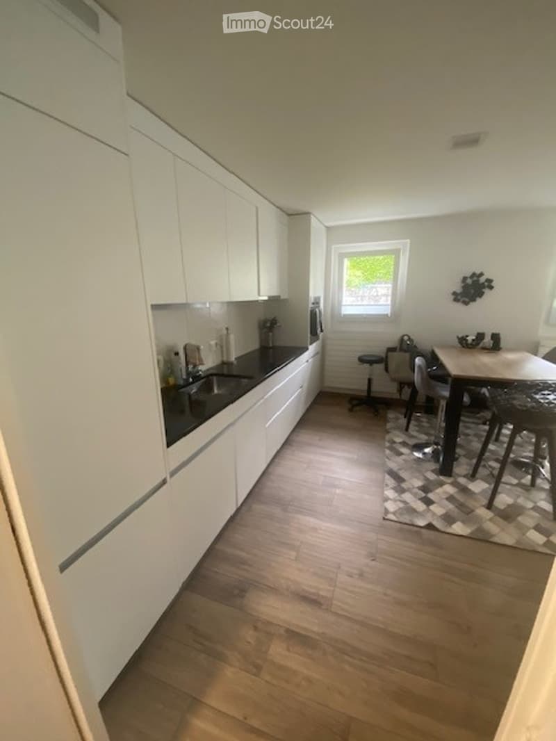 Modern kitchen with white cabinets, wooden flooring, and a small dining area with a table and chairs.