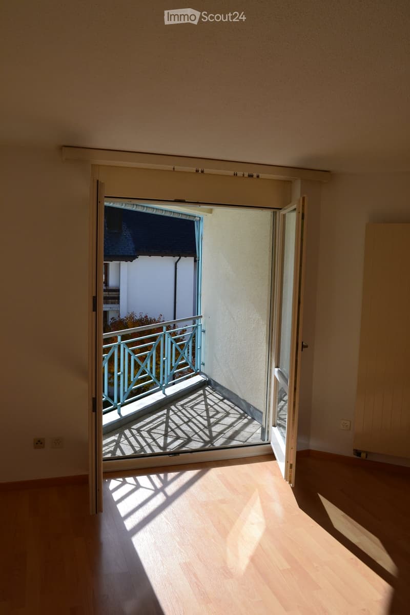 Empty room with wooden flooring, open sliding doors leading to a balcony with a metal railing.