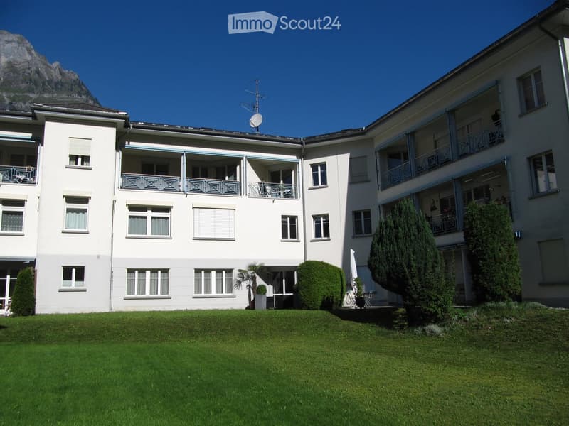A three-story residential building with balconies, large windows, and a well-maintained lawn in front.