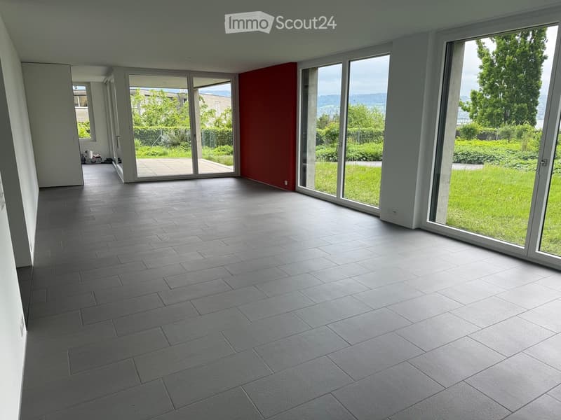 Empty room with grey tiled floor, large glass sliding doors leading to a green outdoor area, white walls, and a red accent wall.