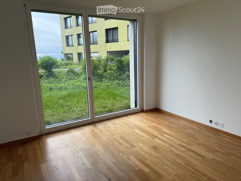 Empty room with wooden flooring and large sliding glass doors leading to a green outdoor area.