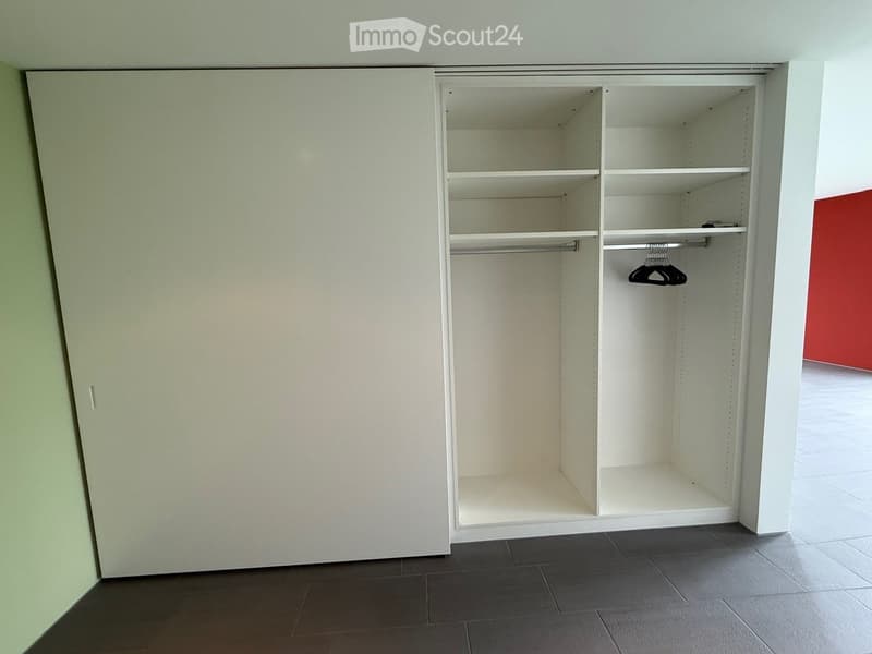Empty room with a built-in closet featuring white shelves and a hanging rod, dark tiled floor, and light-colored walls.