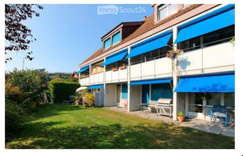 A multi-story residential building with blue awnings, balconies, and a well-maintained lawn in front.