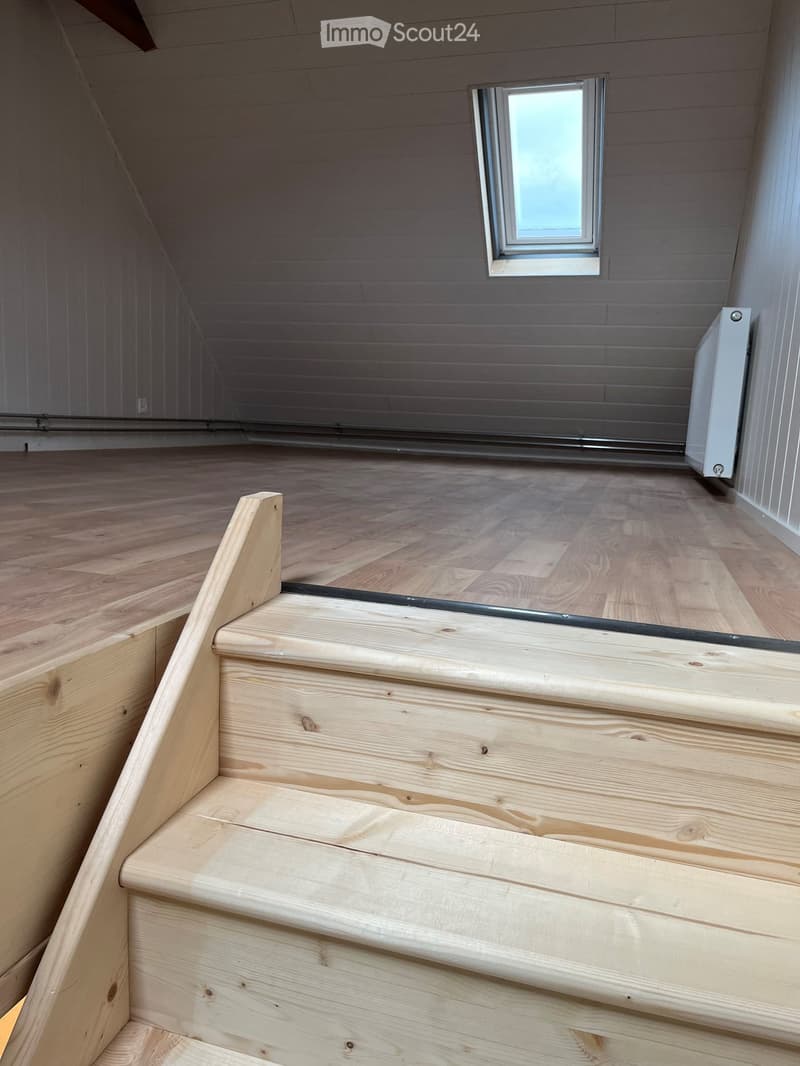 Wooden staircase leading up with a small window at the top, wooden floor, and white walls.