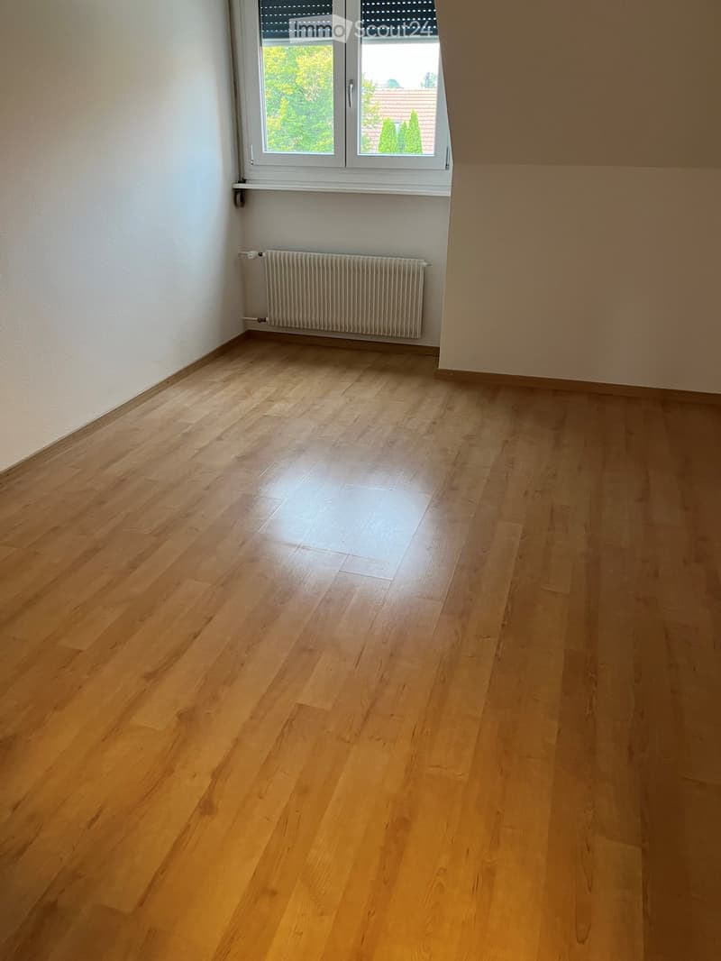 Empty room with light wooden flooring, white walls, a window with blinds, and a radiator below the window.