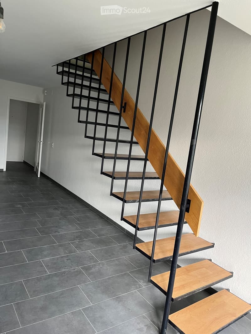 Modern hallway with dark tiled floor, white walls, and a contemporary wooden staircase with black metal frame leading upwards.