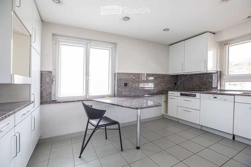 Modern kitchen with white cabinets, granite countertops, tiled floor, and a single chair near the island.
