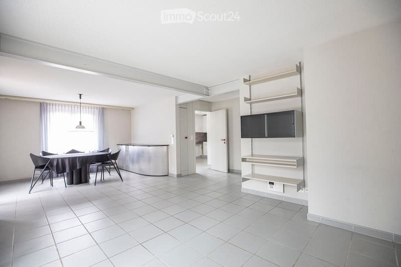 Bright, modern dining area with a round table, four chairs, and built-in cabinets and shelves. The space features white tiled flooring and large windows with sheer curtains.