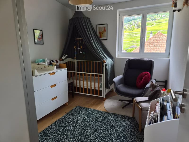 Cozy children's bedroom with a crib, changing table, rocking chair, bookshelf, and a view of a green landscape through a large window.
