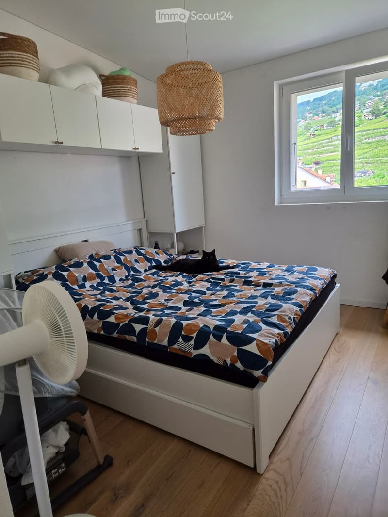 Cozy bedroom with a single bed, a fan, a cat, white cabinets, and a scenic view through a large window.
