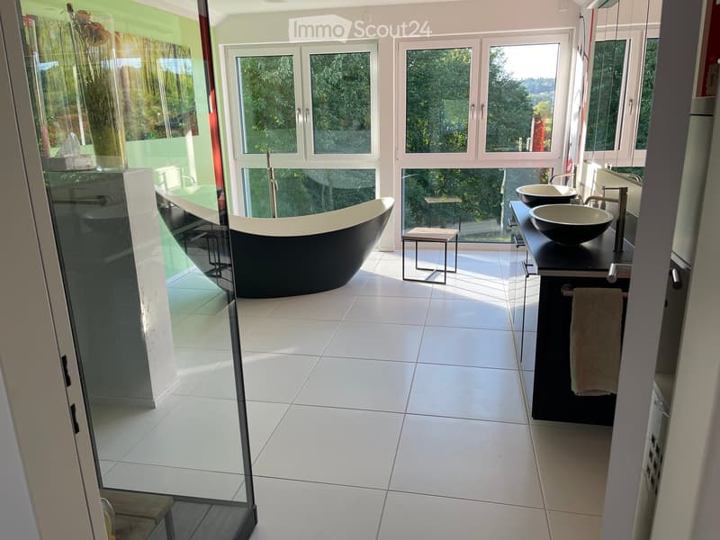 Modern bathroom with white tiled floor, large windows, black bathtub, double sink vanity, and a small stool near the window.