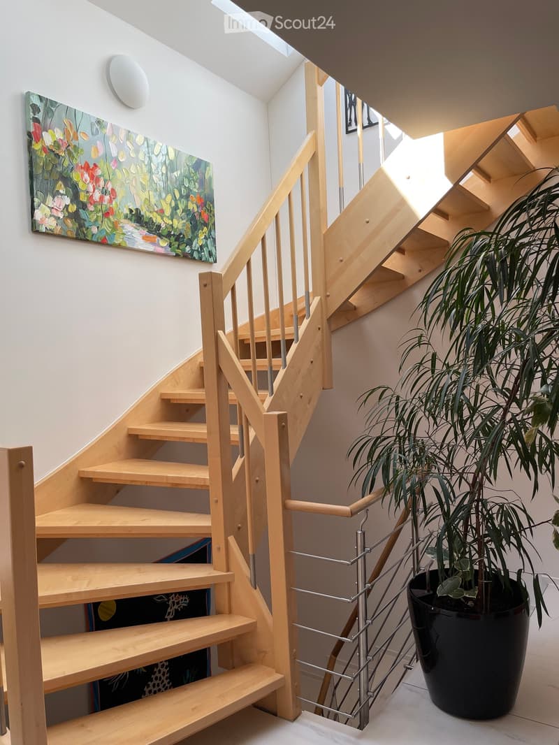 Wooden staircase with metal railing, large potted plant, and abstract painting on wall.
